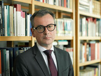 Auf dem Foto steht Rolf-Ulrich Kunze in einem Büro vor einem Bücherregal